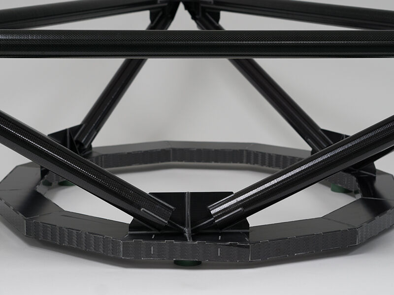 Image shows a closeup of the completed TMT metrology fixture on a white surface and background. The structure is comprised of carbon fiber tubes attached at multiple points by dark metallic fittings. The bottom of the structure is a circular carbon fiber sandwich panel, with carbon plate covering the edges of the sandwich structure.  